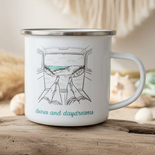 White mug with black rim and handle, featuring a drawing of a train window view and 'dunes and daydreams' text, on a wooden surface.