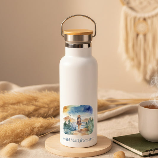 White water bottle with a scenic design and 'wild heart, free spirit' text on a wooden table.