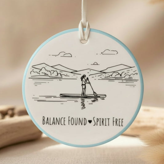Circular pendant with a design of a person paddleboarding and text 'Balance Found Spirit Free' on a light blue background.