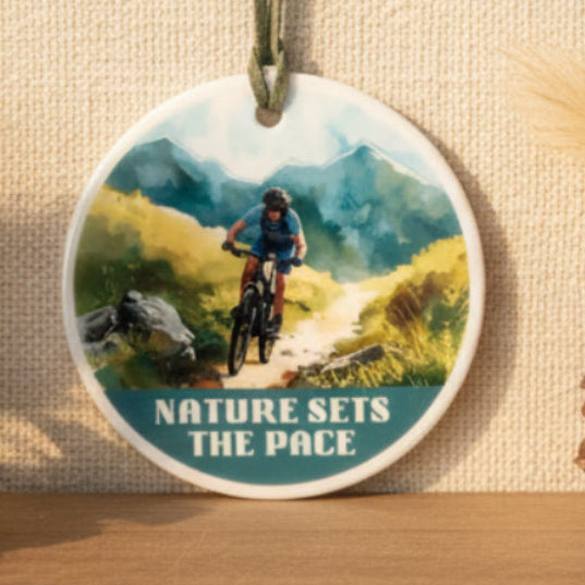Round pendant with a mountain bike design and 'Nature Sets the Pace' text on a white background