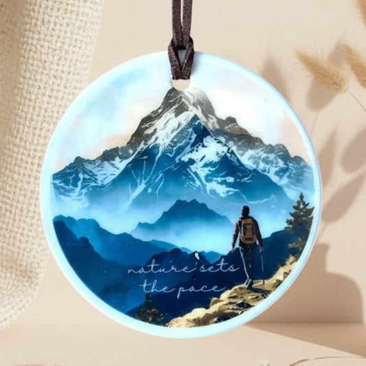 Round decorative item with mountain scene and 'nature sets the pace' text, hanging against a light background.