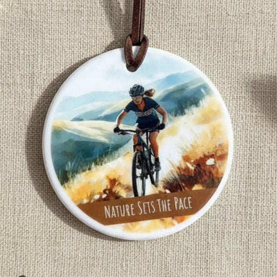 Round pendant with a cyclist design and 'Nature Sets the Pace' text on a plain background