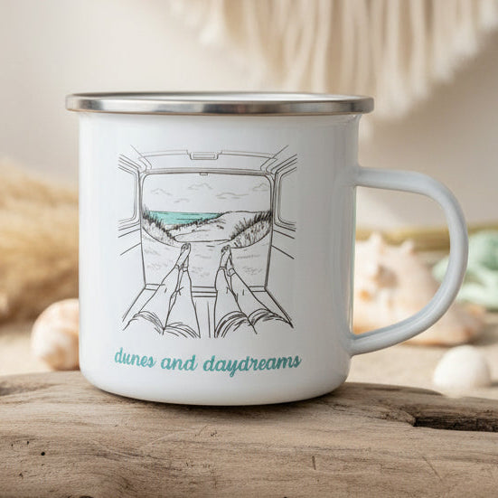 White mug with black rim and handle, featuring a drawing of a train window view and 'dunes and daydreams' text, on a wooden surface.