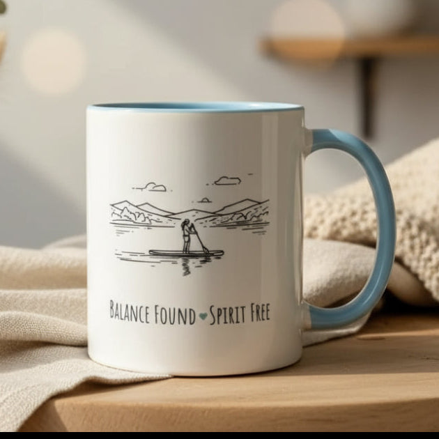 Mug with a design of a person paddleboarding and text 'Balance Found Spirit Free' on a table.