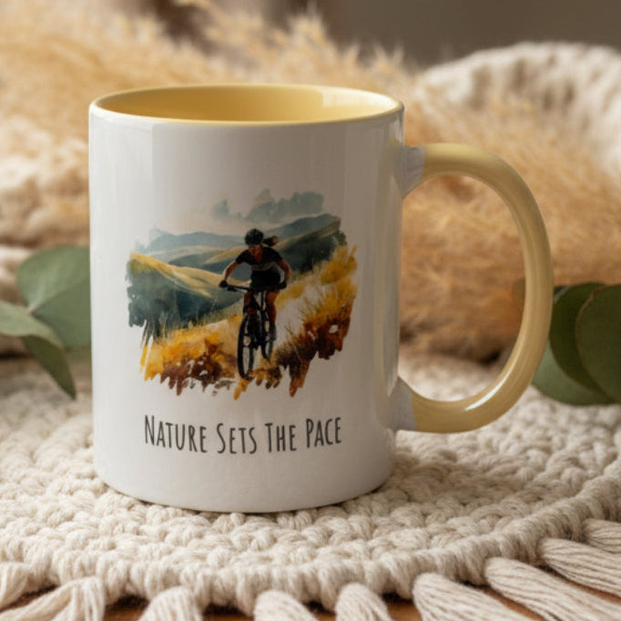 Mug with a cyclist design and 'Nature Sets The Pace' text on a white surface.