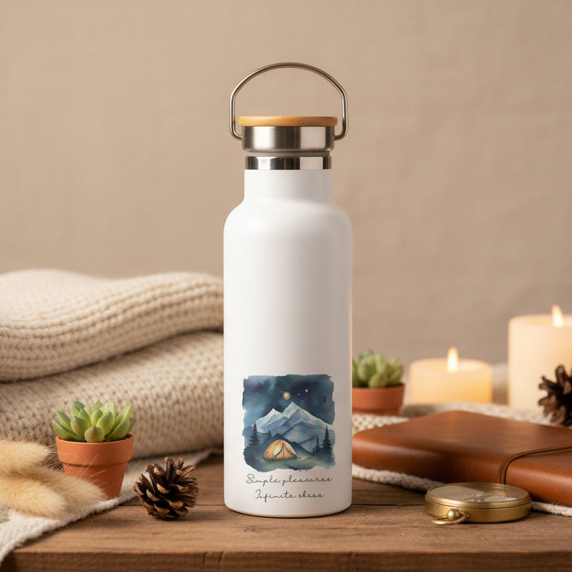 White water bottle with a mountain design on a wooden table with candles and plants.