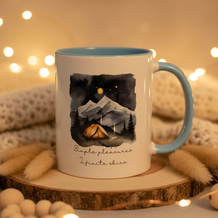 Mug with mountain and tent design and text 'Simple pleasures infinite skies' on a dark background