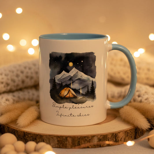 Mug with mountain and tent design and text 'Simple pleasures infinite skies' on a dark background