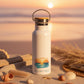 White water bottle with a sunset design and 'Sun Sea Soul' text on a wooden table.