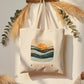 Tote bag with sunset design and 'Sunset Soul' text hanging on a hook against a white wall.