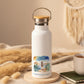 White water bottle with a scenic design and 'wild heart, free spirit' text on a wooden table.